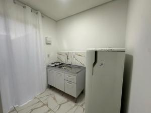 a white kitchen with a refrigerator and a sink at Loft Conteiner in Primavera do Leste
