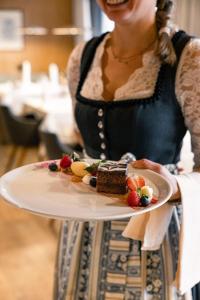 a woman holding a plate with a piece of cake at Granpanorama Hotel StephansHof in Villandro