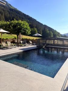 a pool with chairs and umbrellas next to a mountain at Hameau des Prodains - Hôtel in Morzine
