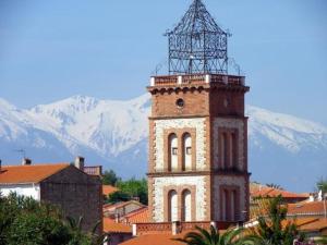 a tall building with a clock tower in front of mountains at 45 Méditerranée in Ortaffa