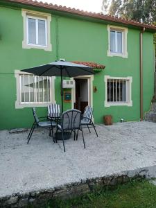a table and chairs with an umbrella in front of a green house at Casa en CEDEIRA in Cedeira