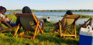 three people sitting in lawn chairs by a lake at Whispering Woods in Kafue