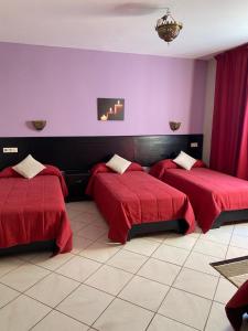 a room with three beds with red covers and purple walls at Hotel Rama in Oued Laou