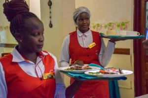 two women holding plates of food in a kitchen at Comfy Inn Hotel in Eldoret
