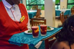 a man holding a tray with two drinks on a table at Comfy Inn Hotel in Eldoret