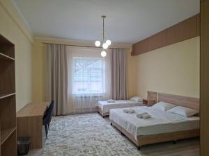 a bedroom with two beds and a desk and a window at Comfort Hotel in Almaty