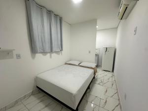 a small white room with a bed and a refrigerator at Loft Conteiner in Primavera do Leste