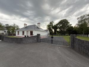 a white house behind a fence with a gate at The Old Post Office Cottage in Castlebar