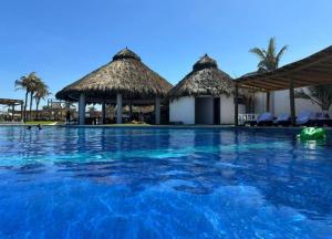 a swimming pool at a resort withiki huts at El descanso del guerrero in Barra Vieja