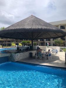 a group of people sitting under a straw umbrella by a pool at Pirâmide Palace Hotel in Natal