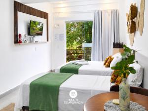 two beds in a room with a table and a window at Pousada Coração do Rosa - Praia do Rosa/SC in Praia do Rosa