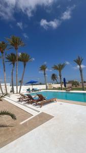 a swimming pool with benches and palm trees at maison rachid in El Guecheïne