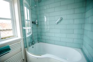 a blue tiled bathroom with a tub and a window at 2 Crown Barton in Glastonbury +45 photos