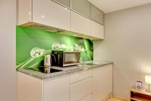 a kitchen with white cabinets and a green wall at Villa Arkodes in Gdańsk