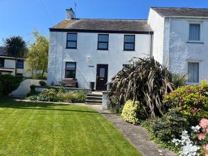 a white house with a yard with flowers at Coastal Charm Seaside House in Moelfre