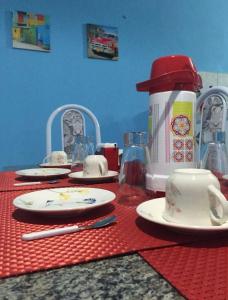 a table with a red table cloth with plates and a coffee maker at Casinha de vó in Aracati +19 photos