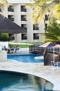a pool at a resort with palm trees and chairs at Pirâmide Palace Hotel in Natal