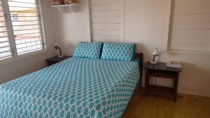 a bedroom with a bed with a blue comforter and a table at Tri Tan Beach Cabanas in Placencia