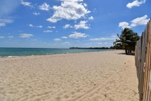 a beach with a fence and trees and the ocean at Tri Tan Beach Cabanas in Placencia +2 photos