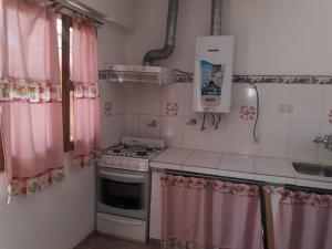 a small kitchen with pink curtains and a stove at Departamento Los Rosales in Villa Cura Brochero