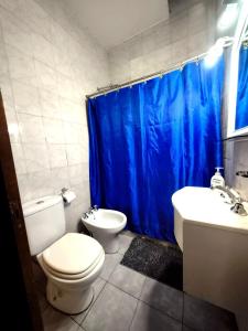 a bathroom with a toilet and a blue shower curtain at La Casa de Pilar - Casa Completa con Cochera y Patio in San Juan +3 photos