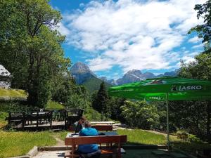 two people sitting at a table under a green umbrella at Planinski dom Hermanov Hram in Log pod Mangartom