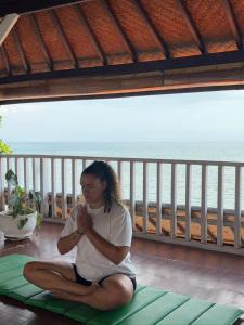 a woman sitting on a yoga mat in front of the beach at Villa Agung Beach Inn in Lovina
