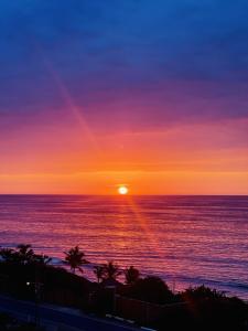 a sunset over the ocean with palm trees at La Cabaña de Iza in Canoas