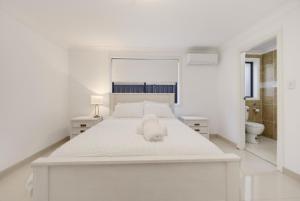 a white bedroom with a white bed and a toilet at Sapphire By The Sea in Diamond Beach