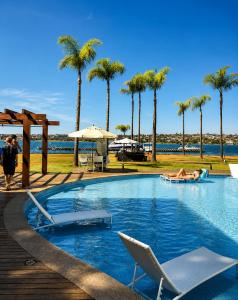 a swimming pool with chairs and palm trees on a beach at Comfortable Serviced Apartment by the Lake in Brasília