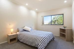 a white bedroom with a bed and a window at Kyeema in Tathra