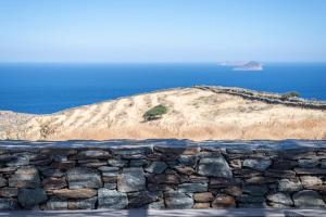 a stone wall in front of a hill with the ocean at Ayelma - Kythnos Villa in Kithnos