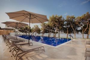 a row of chairs with umbrellas next to a swimming pool at Hotel Punta in Vodice