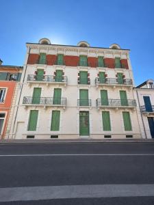 a tall white building with green doors and windows at The Originals Residence, Les Sources Callou, Vichy in Vichy