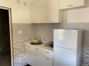 a white kitchen with a sink and a refrigerator at Apartmani Ličina in Bečići +7 photos