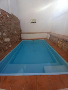a blue swimming pool in a room with a stone wall at La Casa del Abuelo Curro in Baños de la Encina