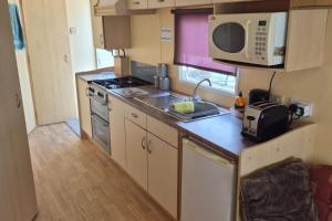 a small kitchen with a sink and a microwave at Cabin Sleeps 6 with access outdoor Pool in Sandown