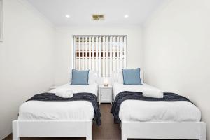 two beds in a white room with blue pillows at 4 bedroom luxury modern home near the beach and parks in Alkimos +35 photos
