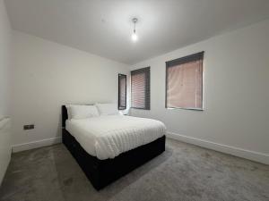 a bedroom with a bed with white sheets and two windows at Serene 2-BDR Maisonette in Wolverhampton