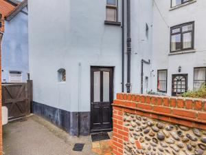 a white building with a door and a brick wall at Melrose Cottage in Cromer