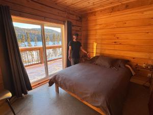 a man standing next to a bed in a room with a window at Auberge Boréale de Charlevoix in Petit-Saguenay