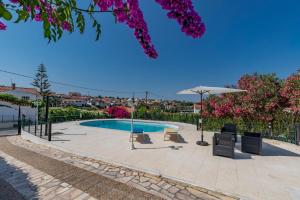 a swimming pool with chairs and an umbrella at Vivenda Verivitor - Saltwater Pool, Garden, BBQ & Tennis Court in Sesimbra