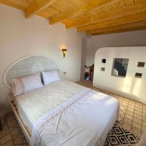 a bedroom with a white bed with a wooden ceiling at Houch Taguermess in Taguermess