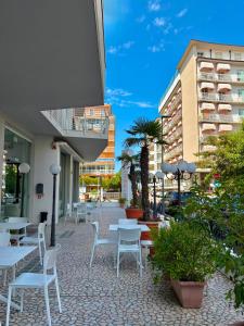 a patio with white tables and chairs and buildings at Hotel Aragosta in Cattolica