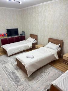 a room with two beds and a tv on a wall at DARAI guest house Hostel Turkistan in Türkistan