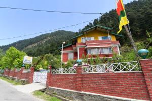 a house behind a brick fence with a flag at Hotel O by OYO Manali Meadows Home Stay in Manāli