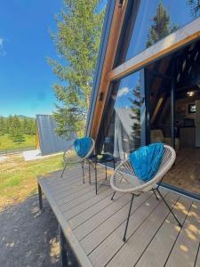 two chairs sitting on a wooden deck in front of a house at Forest Whisper Lux - A-frame cabin with private hot tub in Kovačka Dolina