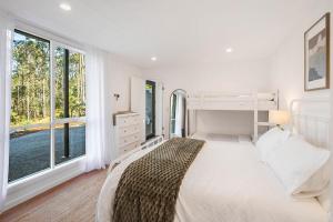 a white bedroom with a bed and large windows at Maisie's in Tathra