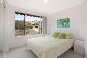 a white bedroom with a bed and a window at Holiday on Pacific in Tathra