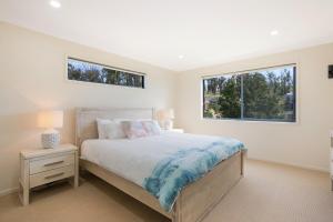 a white bedroom with a bed and two windows at Fanta Sea in Tathra